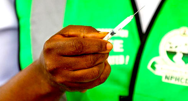 A health worker holds a vaccine tube and a syringe.