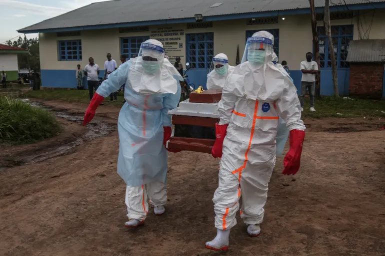 Medical staff wearing personal protective equipment (PPE) carry the body of a patient deceased at the hospital in Rwampara, DRC towards the cemetery on May 21, 2026 [AFP]